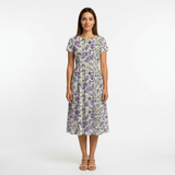 Woman in a white cotton lawn dress with purple floral print, short sleeves, and a gathered waist.