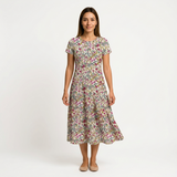 Woman in a white cotton floral print midi dress with pink, green, and yellow flowers.