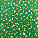 A folded piece of green fabric with a small repeating floral print in yellow, red, and white, laid flat on a brown wooden surface.