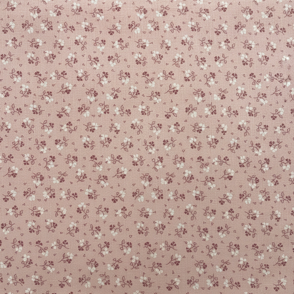 A folded piece of fabric with a dense small floral print in muted pink and green on an off-white background, laid flat on a dark wood surface.