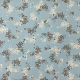 A light blue fabric with a brown and cream floral pattern, laid flat on a dark brown wooden surface.