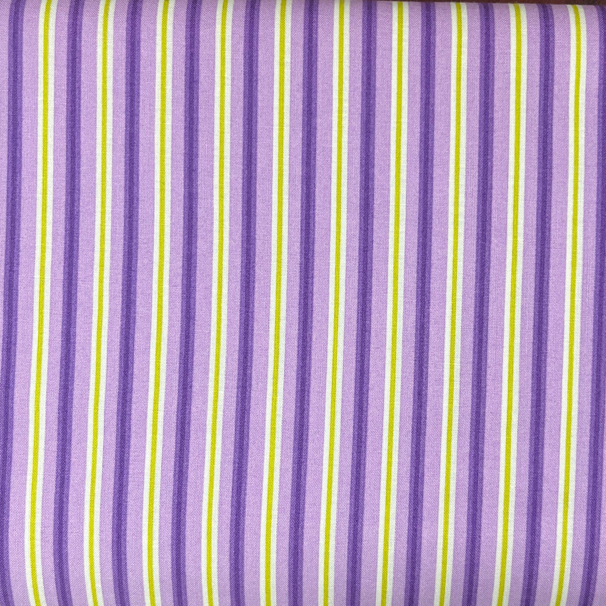 A folded piece of fabric with a purple, white, and lime green striped pattern, laid flat on a dark wood surface.