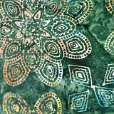 A close-up of a batik fabric featuring a green marbled background with hand-drawn mandala and geometric patterns in white, yellow, and orange.
