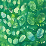 A close-up of a batik fabric or paper pattern featuring organic, teardrop-shaped spots in shades of light blue, purple, and pink over a textured teal and turquoise background.