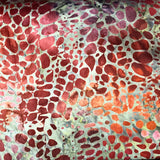 A close-up of a batik fabric with a red, orange, and beige spotted pattern, layered over other batik fabrics.