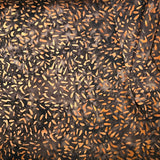 A close-up of a folded brown fabric with a dense black and orange speckled pattern, layered over other colorful patterned textiles.