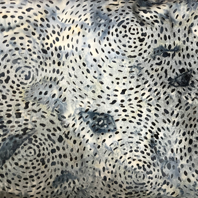 A close-up of a patterned fabric with a black spiral dot design on a white base, layered over other colorful patterned fabrics.