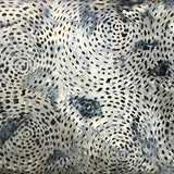 A close-up of a patterned fabric with a black spiral dot design on a white base, layered over other colorful patterned fabrics.