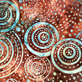 A close-up of a batik fabric with a brown, orange, and blue circular dot pattern, held by a hand.