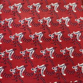 A close-up of a folded red fabric, likely cotton block-printed cotton fabric, featuring a repeating white and dark brown floral or paisley pattern.
