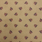 A close-up of a beige necktie featuring a fine grid pattern and a repeating dark floral motif, held by a hand.