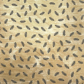 A close-up of a beige fabric with a repeating pattern of small black feather-like shapes, laid flat on a dark wooden surface.