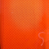Close-up of a bright orange perforated fabric or mesh material with a small repeating hole pattern, photographed indoors with some surrounding objects visible at the edges.
