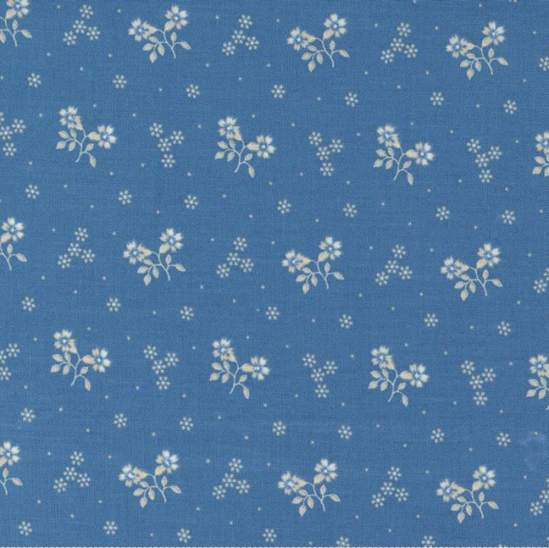 Blue fabric with a repeating white floral and dot pattern, shown flat with a ruler along the bottom edge for scale. The brand name 'moda' is visible at the bottom.