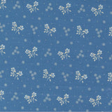 Blue fabric with a repeating white floral and dot pattern, shown flat with a ruler along the bottom edge for scale. The brand name 'moda' is visible at the bottom.