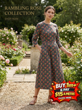 Woman in a grey Rambling Rose floral print dress with 3/4 sleeves, standing in a rose garden.