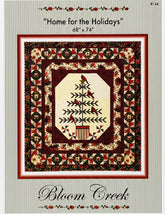 Bloom Creek 'Home for the Holidays' counted cross-stitch pattern in its original clear plastic packaging, featuring a festive quilted design with a central Christmas tree motif.