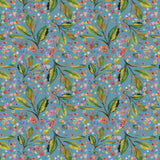 A close-up of a floral fabric pattern featuring green leaves and small pink, yellow, and white flowers on a dusty blue background, with a wooden ruler along the bottom edge showing measurements.