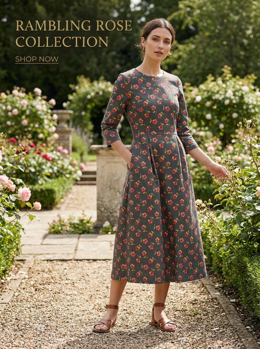 Woman in a grey Rambling Rose floral print dress with 3/4 sleeves, standing in a rose garden.