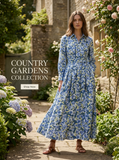 Woman in a blue floral long-sleeve maxi dress with a belted waist, standing in a garden path.