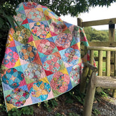 Colorful patchwork quilt with floral circle blocks and square sashing, draped over a wooden fence.