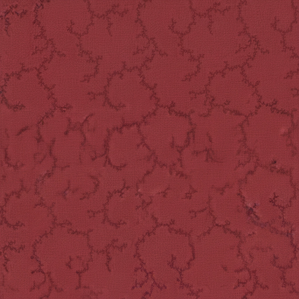 A close-up of a red fabric with a repeating dark red trellis or floral vine pattern, shown with a white ruler along the bottom edge for scale. The brand name 'moda' and website 'www.