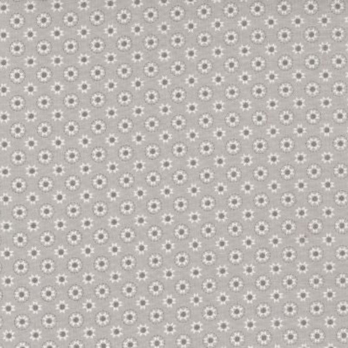 A close-up of a fabric pattern showing a repeating small floral or daisy-like motif in light gray on a slightly darker gray background, with a ruler along the bottom edge and Modas Fabrics branding visible.