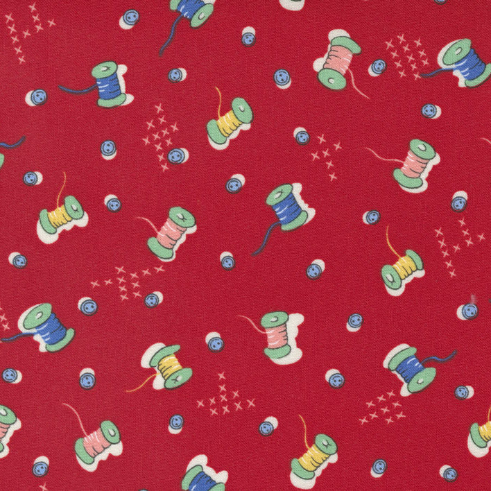 Red fabric with a repeating pattern of colorful thread spools and small starburst motifs.