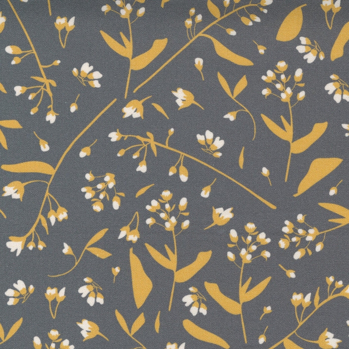 A close-up of a fabric pattern featuring delicate white flowers and mustard yellow leaves on a dark gray background, with a white ruler at the bottom showing measurement markings and the Moda brand name.