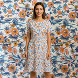 Woman wearing a white cotton dress with a vibrant orange, pink, and blue floral print.