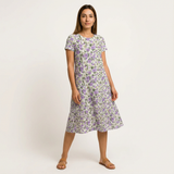 Woman in a white cotton midi dress with a purple floral print, short sleeves, and a round neck.