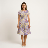 Woman in a short-sleeve cotton dress with a vibrant yellow and purple floral print.