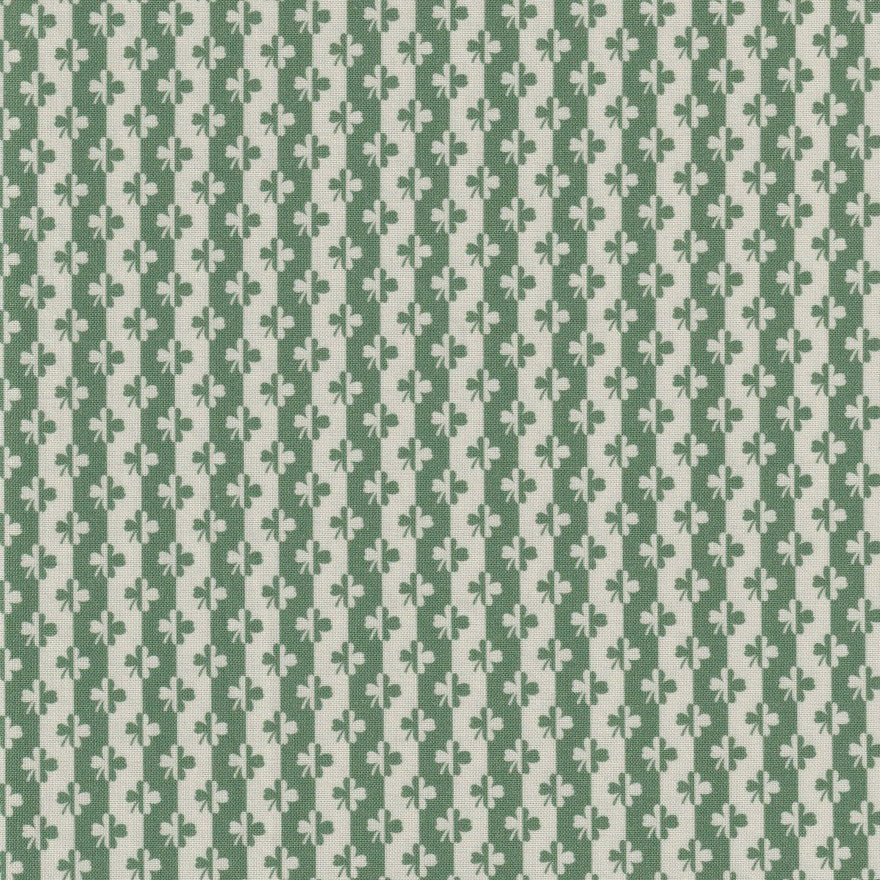 A close-up of a fabric pattern featuring vertical stripes of sage green and cream with a repeating stylized floral or leaf motif, with a measuring ruler visible along the bottom edge.