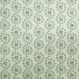 A close-up of a fabric pattern featuring a repeating design of green and brown floral medallions on a white background with fine black speckles.