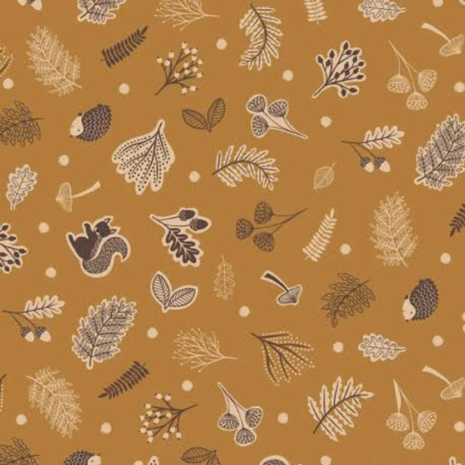 A close-up of a fabric pattern featuring autumn leaves, acorns, pinecones, mushrooms, and squirrels in brown, beige, and cream on a warm mustard-brown background, with a white ruler at the bottom showing scale.