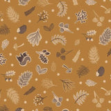A close-up of a fabric pattern featuring autumn leaves, acorns, pinecones, mushrooms, and squirrels in brown, beige, and cream on a warm mustard-brown background, with a white ruler at the bottom showing scale.