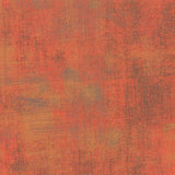 A close-up of a textured surface with a mottled, distressed pattern in warm rust, terracotta, orange, and brown tones.