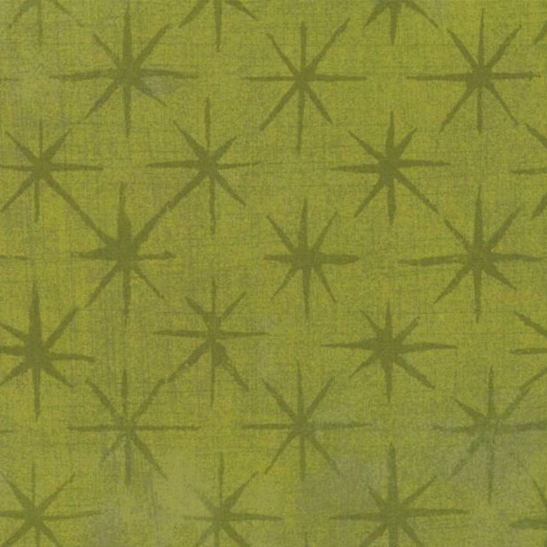 A close-up of a fabric or wallpaper pattern featuring a repeating dark olive green eight-pointed starburst on a textured yellow-green background.