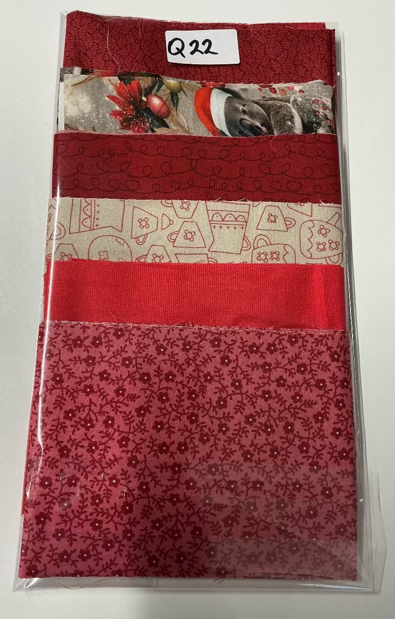 A packaged set of red and festive patterned fabrics or mats in a clear plastic sleeve, photographed on a plain white surface. The set includes solid red, floral red, and cream patterns with holiday motifs.