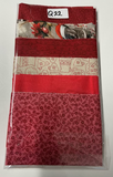 A packaged set of red and festive patterned fabrics or mats in a clear plastic sleeve, photographed on a plain white surface. The set includes solid red, floral red, and cream patterns with holiday motifs.