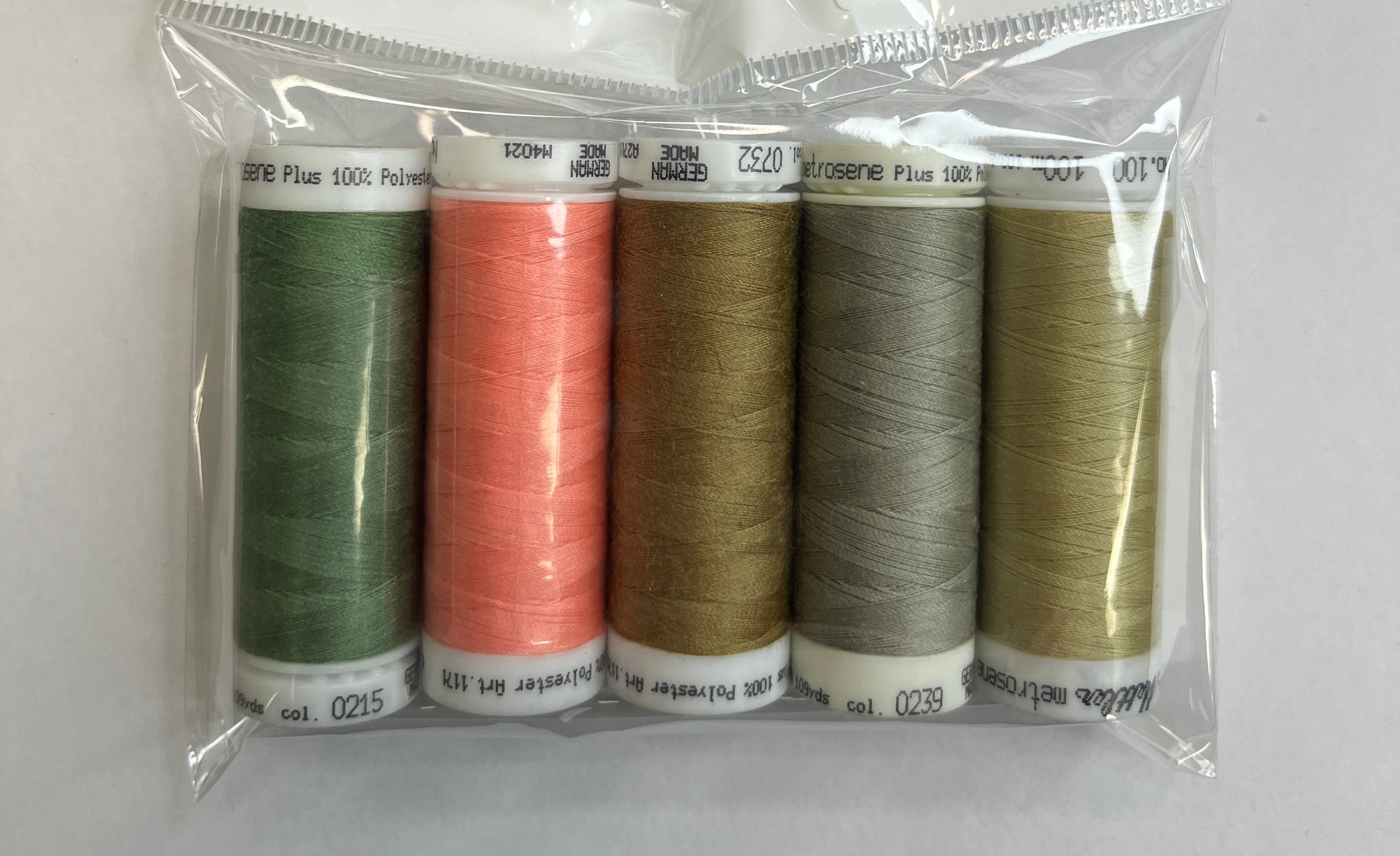 Set of five spools of thread in various colors in a clear plastic package with a white background.