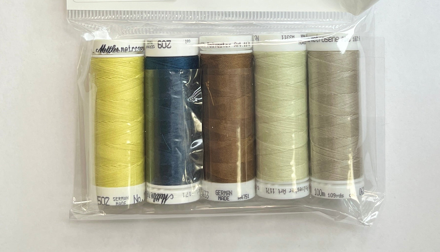 Set of thread spools in a clear package on a wooden surface with a floral-patterned object in the corner.