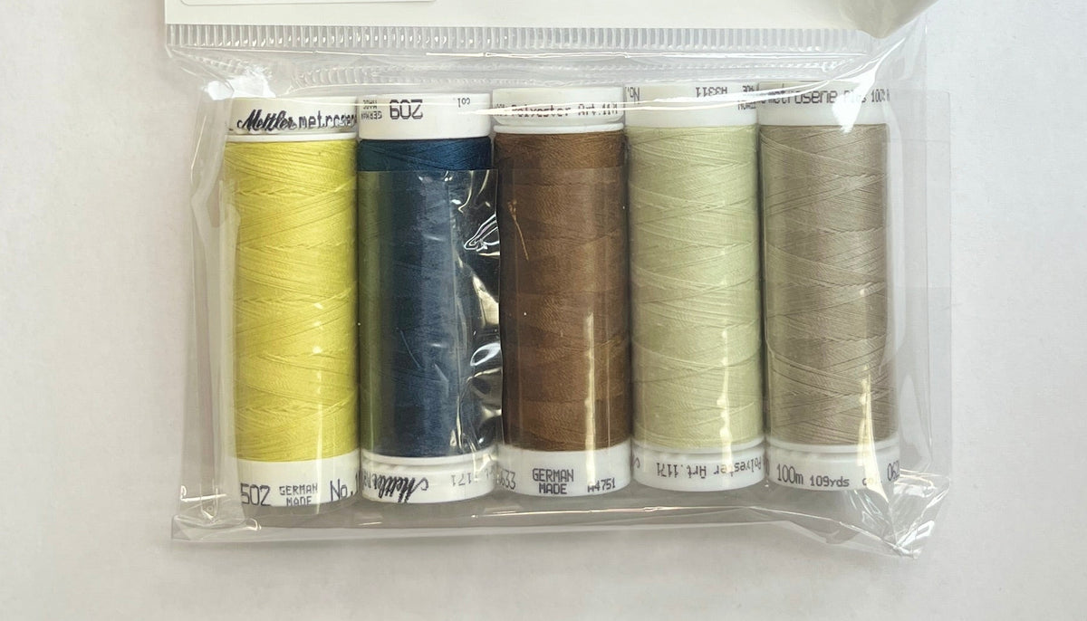 Set of thread spools in a clear package on a wooden surface with a floral-patterned object in the corner.
