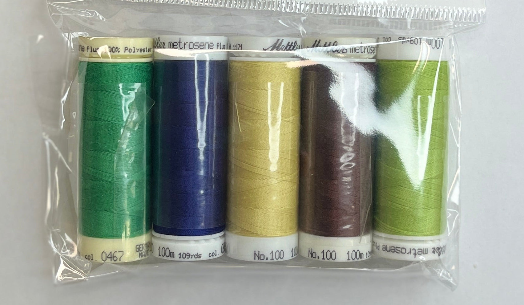 Set of colorful thread spools in a clear package on a white sheet with a pen and fabric swatch.
