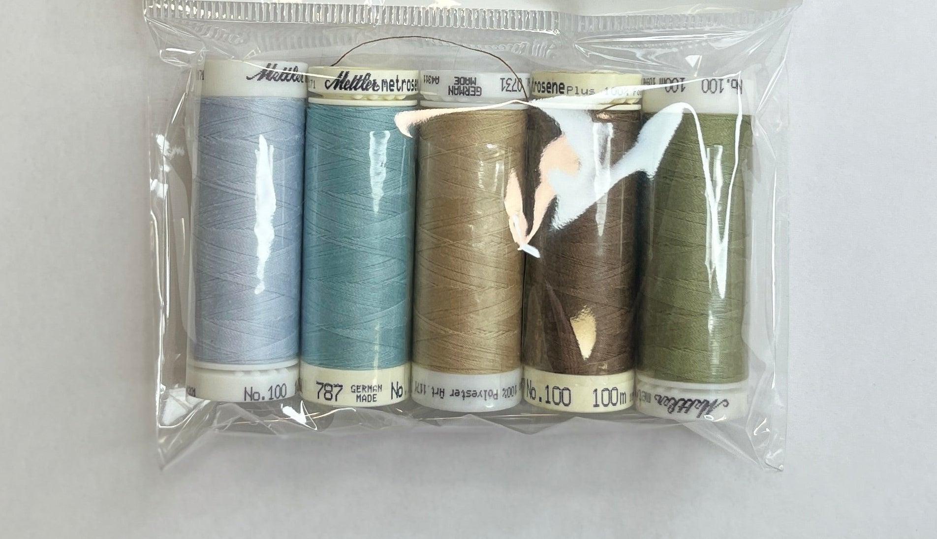 Set of thread spools in a clear package on a white sheet with a wooden surface.