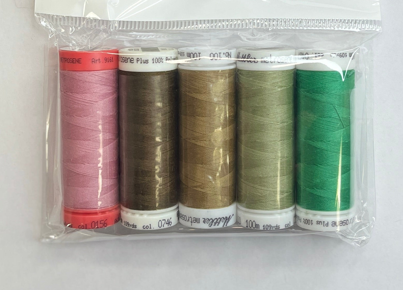 Set of colorful thread spools in a clear package on a white sheet with a pen and floral-patterned object.
