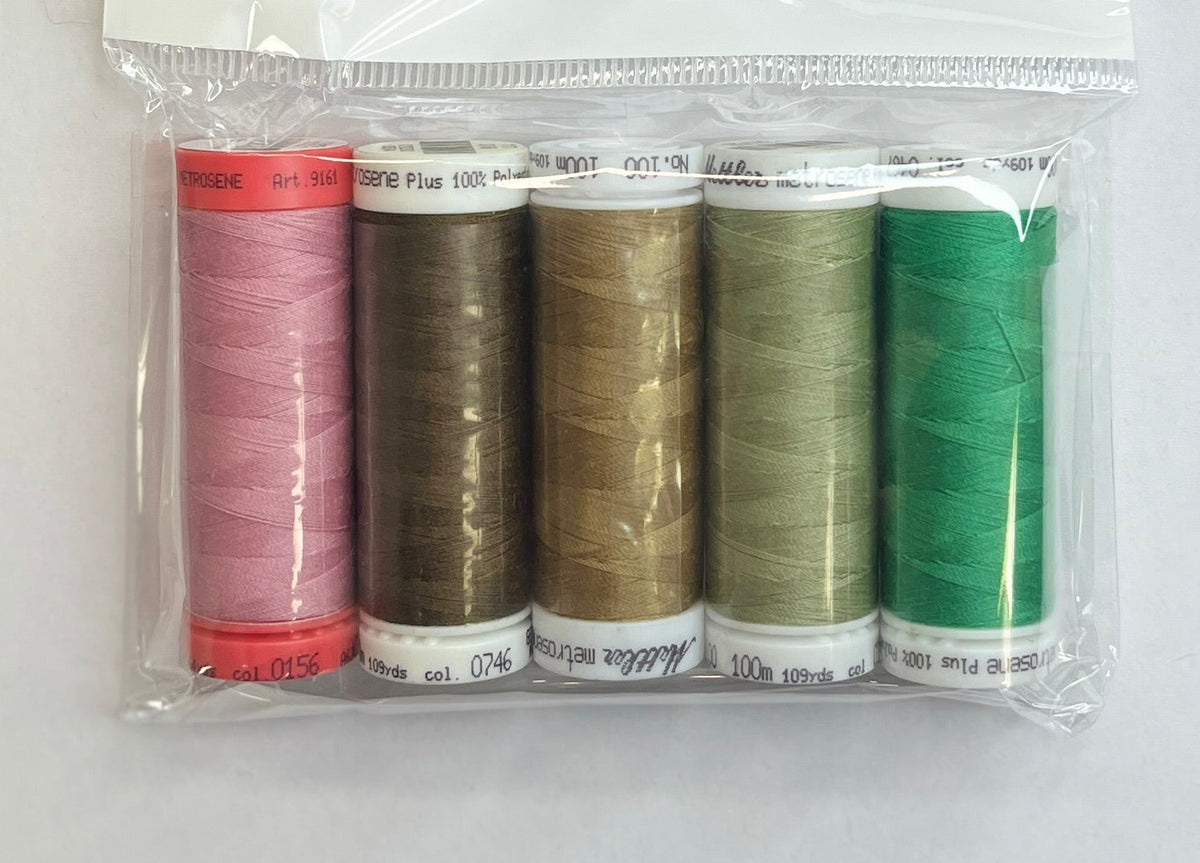 Set of colorful thread spools in a clear package on a white sheet with a pen and floral-patterned object.