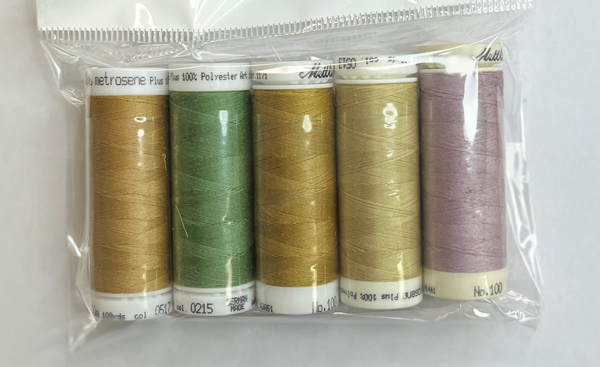 Set of thread spools in a clear package on a white surface with a pen and floral-patterned object.