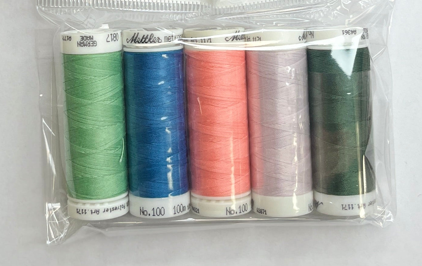 Set of colorful thread spools in a clear package on a white sheet of paper with a wooden surface.