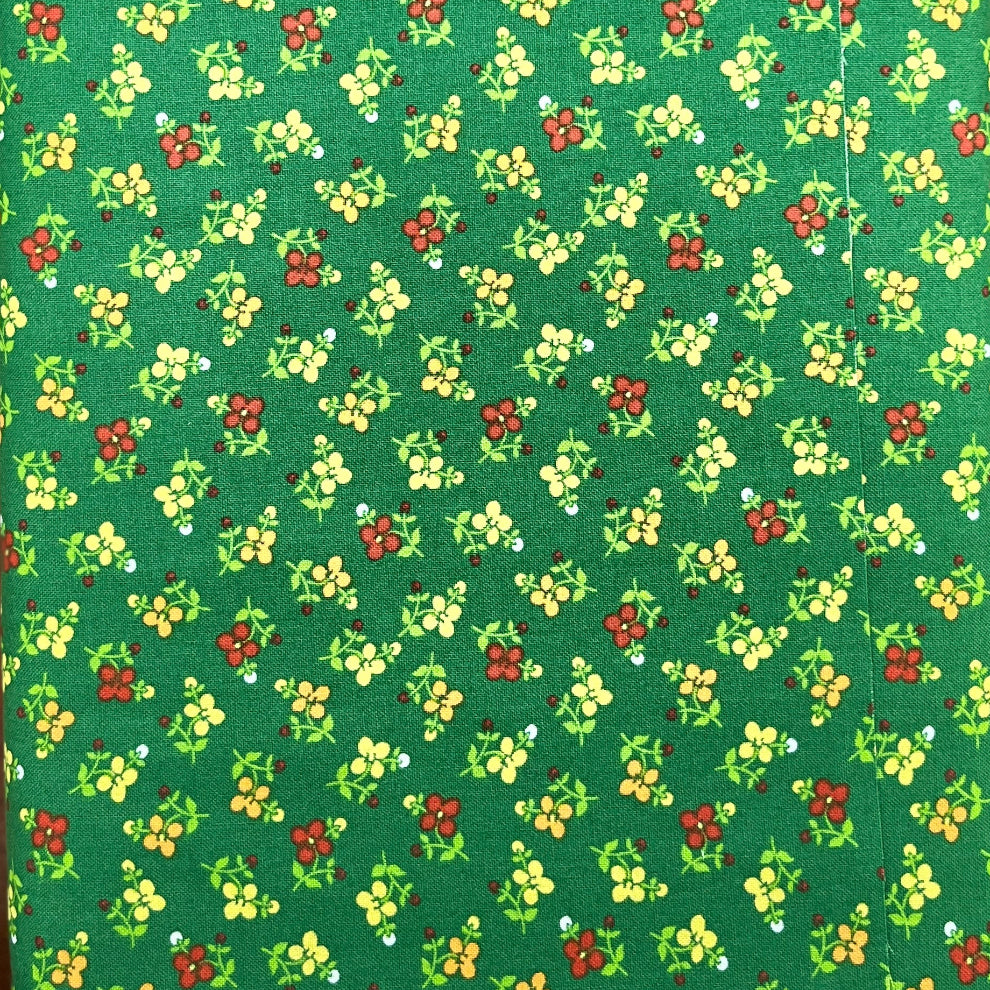 A folded piece of green fabric with a small repeating floral print in yellow, red, and white, laid flat on a brown wooden surface.